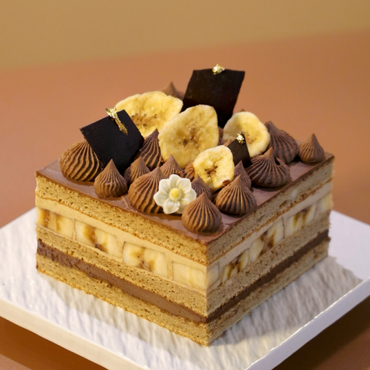 A premium gluten-free Banana and Mocha Layer Cake topped with crispy banana chips and dark chocolate shards, handcrafted by BLUEBUTTER Patisserie in Perth.