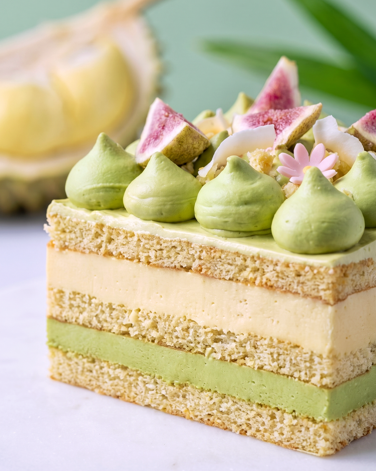 Close-up of BLUEBUTTER’s D24 durian and pandan layer cheesecake with pandan cream and fig garnish.