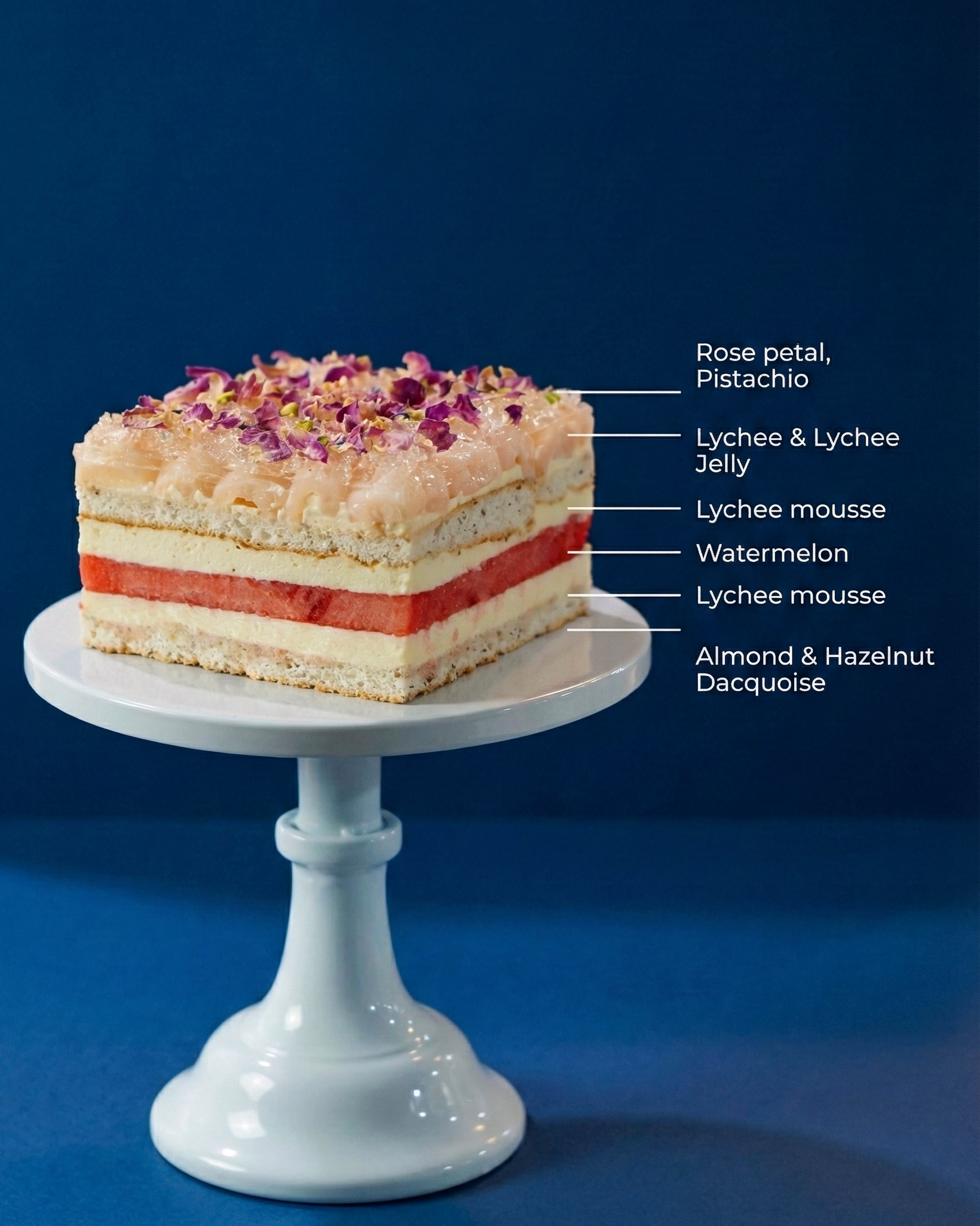Cross-section of an elegant fresh fruit cake showing crisp watermelon, lychee rose crémeux, and a soft toasted hazelnut base.